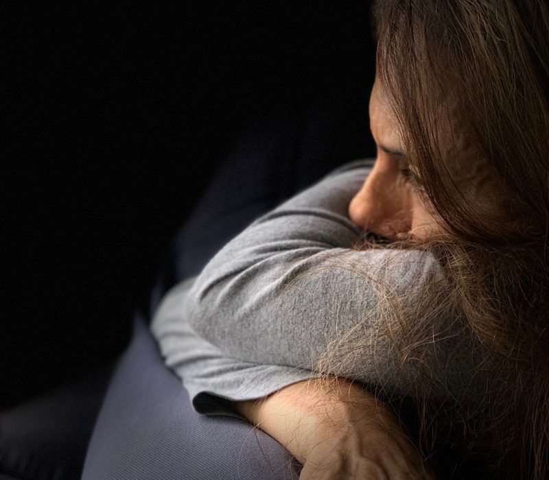 Woman in despair helpless seating in the dark looking sad depressed and lost in thoughts